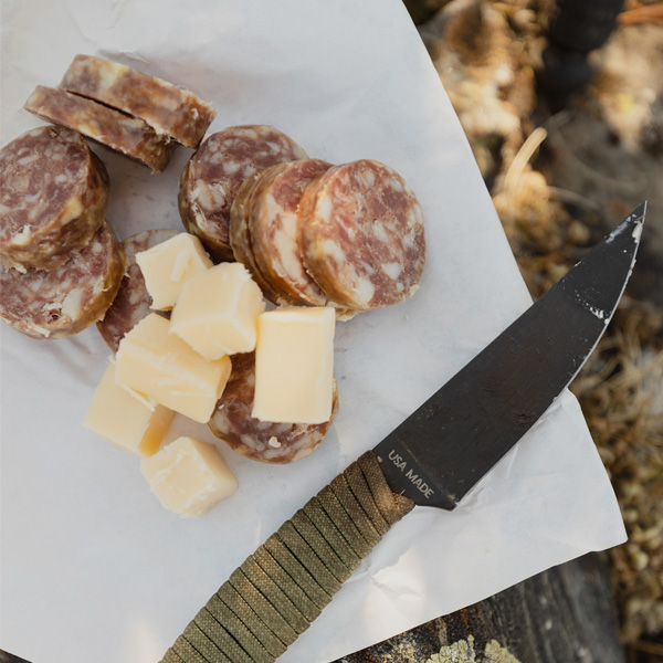 salami and cheese with a small knife cut up on a stump
